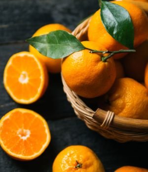 Juicy bright ripe tangerines in wooden basket on dark background